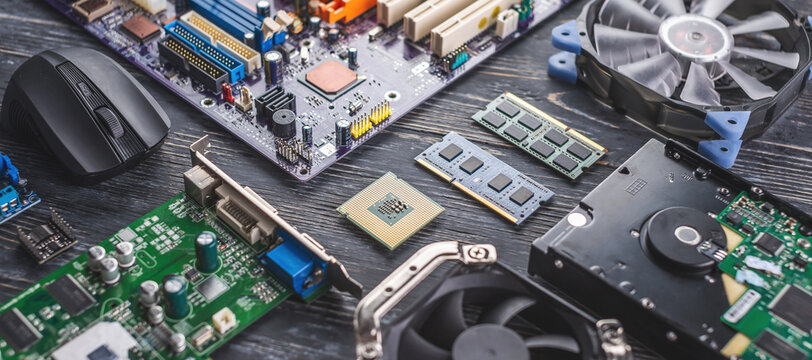 computer hardware components laid out on a wooden surface, including a motherboard, CPU, RAM sticks, cooling fan, graphics card, hard drive, and a black mouse. These components, essential for custom PC building or repair in Dublin, are arranged to emphasize the complexity and variety of parts involved in delivering top-tier PC repair services.